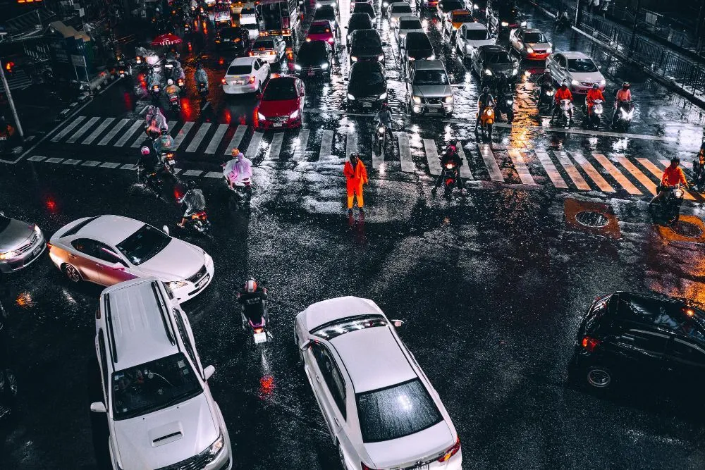 Night scene of traffic congestion in a wet urban area; cars and motorcycles on a rain-slicked road.