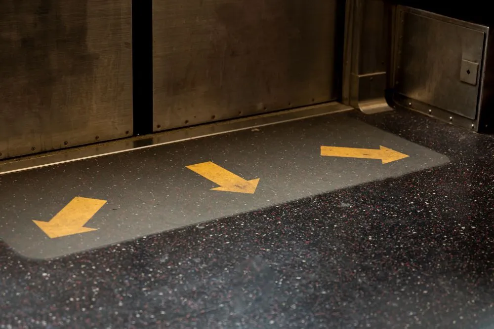 Yellow arrows on a floor mat inside a subway car point towards the right, guiding passengers.