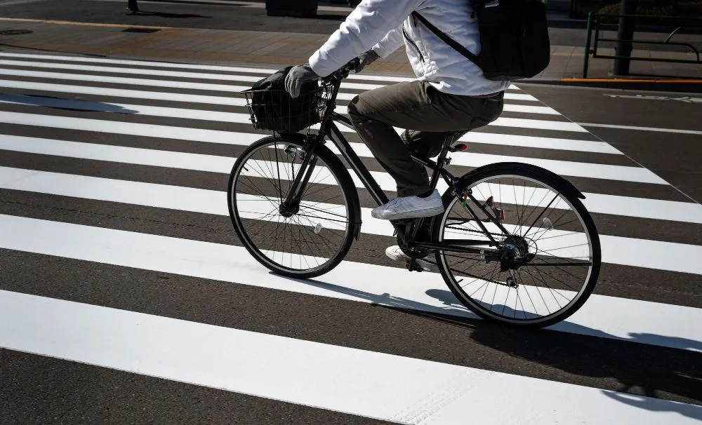Cyclist on black bicycle crossing a white crosswalk. Sunny day.