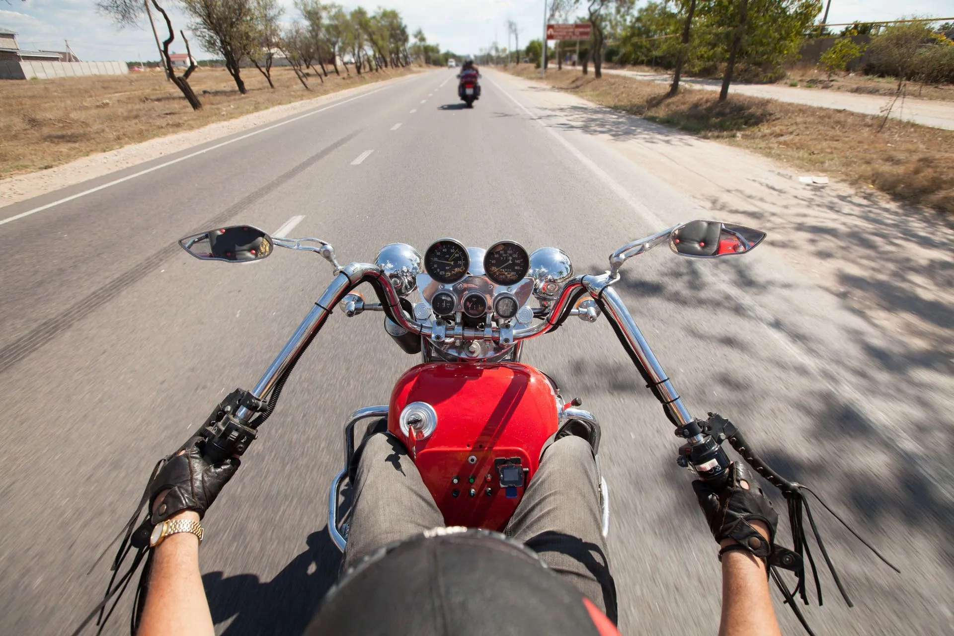 Motorcycle rider on a red chopper follows another on a highway; sunny day.