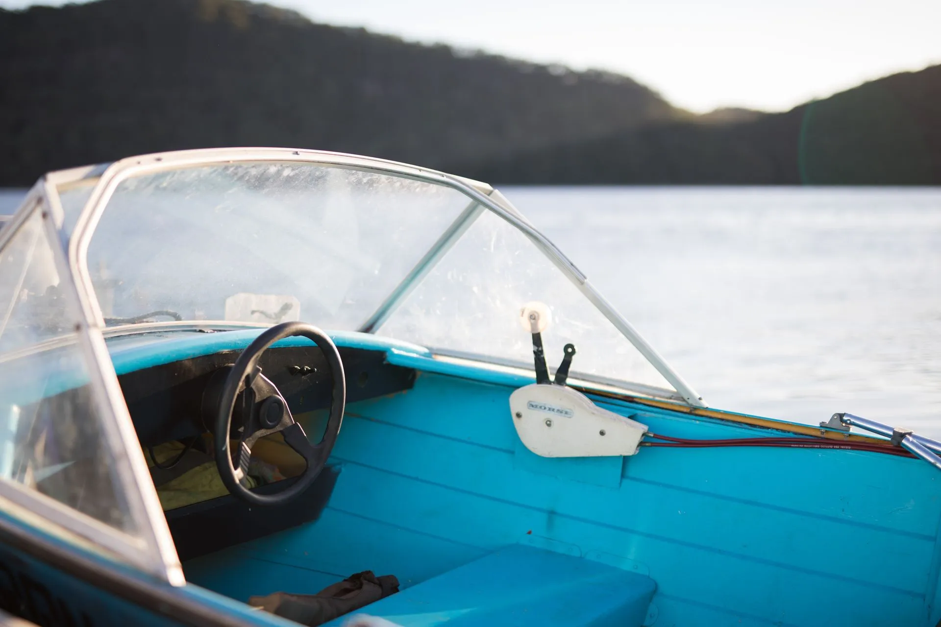 Teal boat interior with steering wheel, windshield, and a lake in the background.