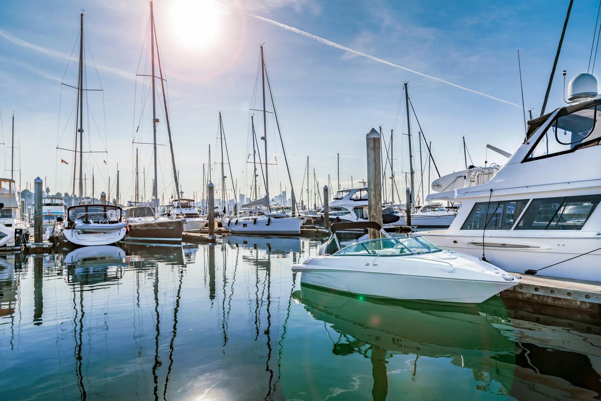 Boats docked in a sunny harbor, masts and reflections in the water.