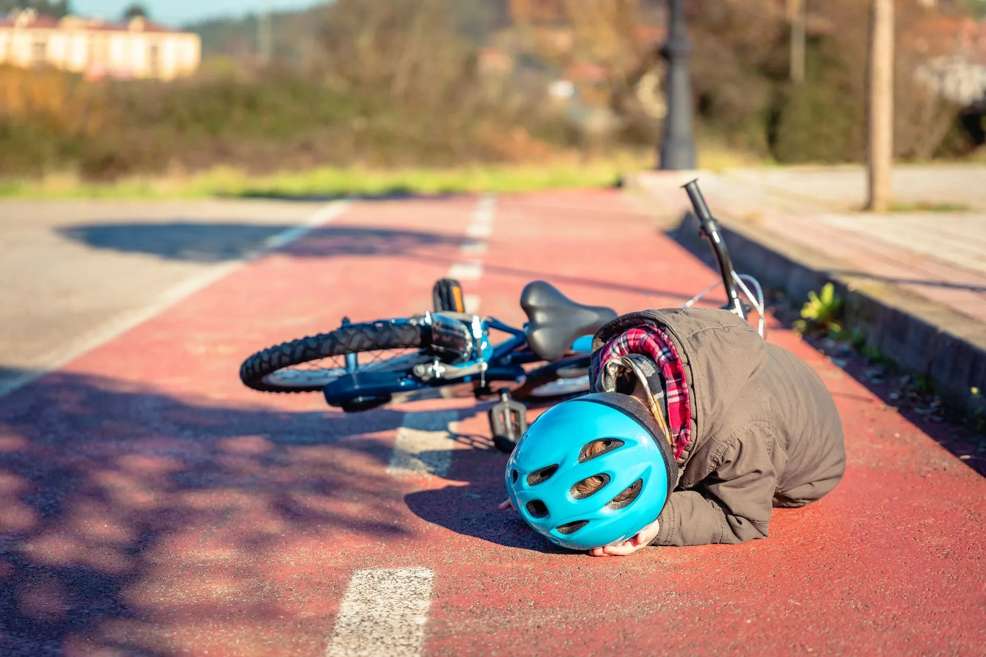 Person on the ground after a bicycle crash, wearing a helmet on a red bike path next to the curb.