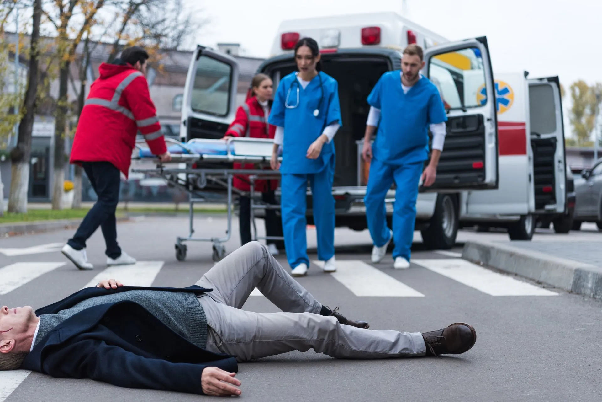 Man lying on a crosswalk; medical personnel tending to him near an ambulance.