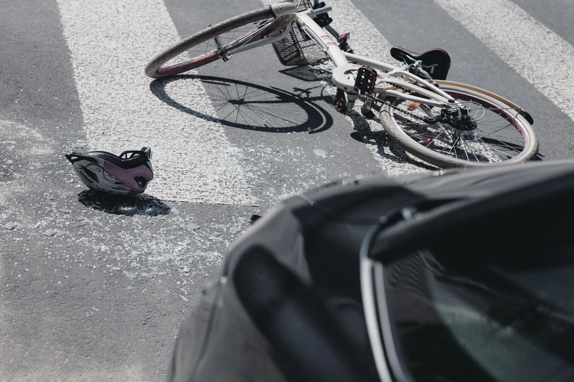 Bicycle and helmet on a crosswalk after a collision with a black car.