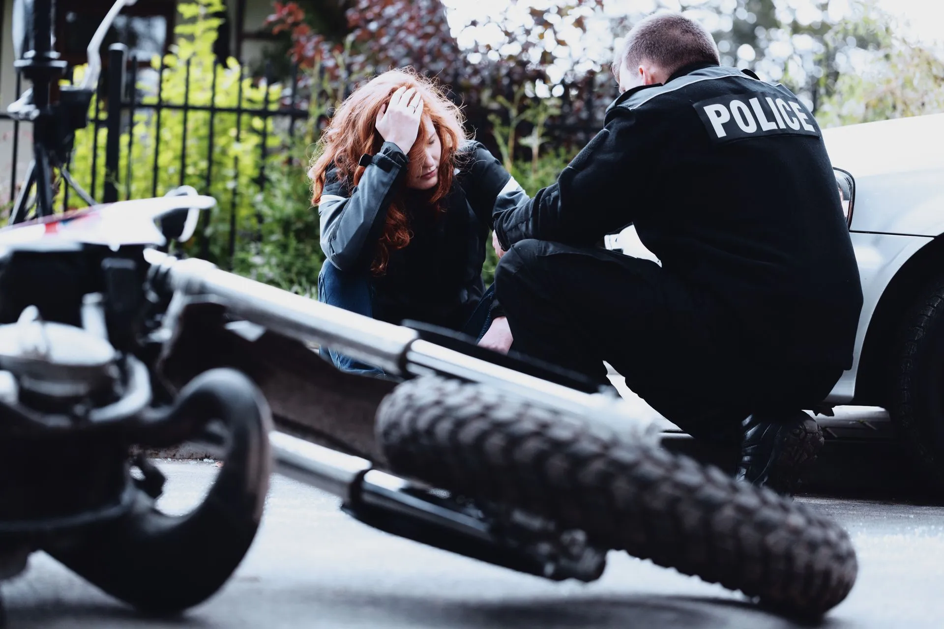 A woman with red hair reacts near a crashed motorcycle as a police officer kneels beside her.