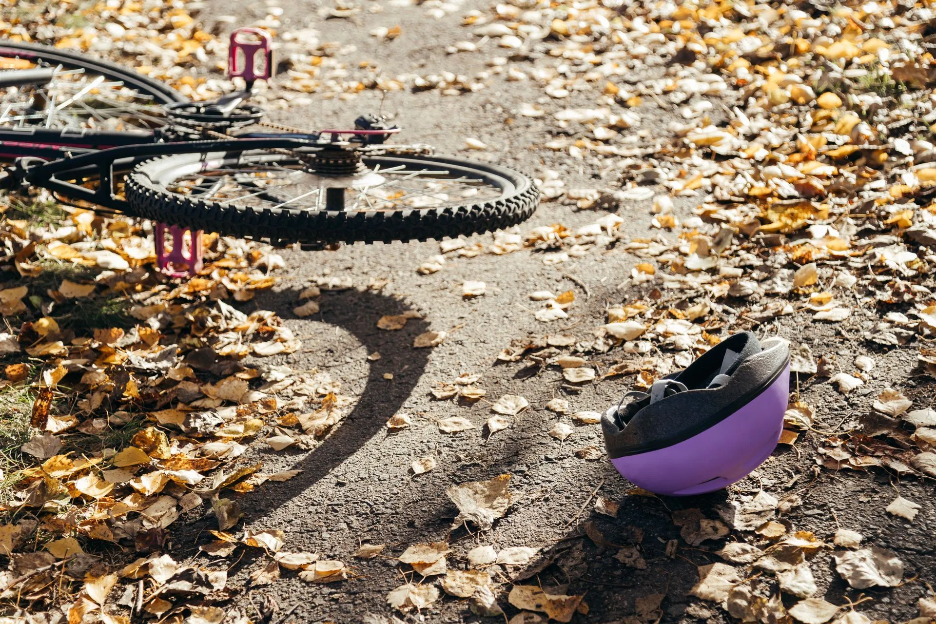 Bicycle lying on a path covered in leaves with a purple helmet nearby.