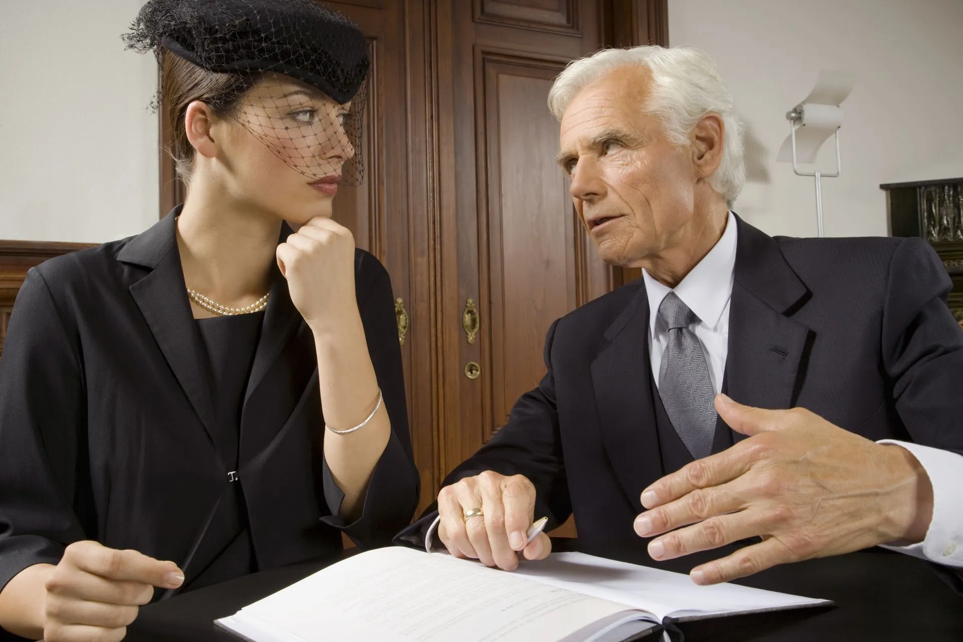 Woman in mourning attire consults with a man in a suit, possibly an attorney, indoors.